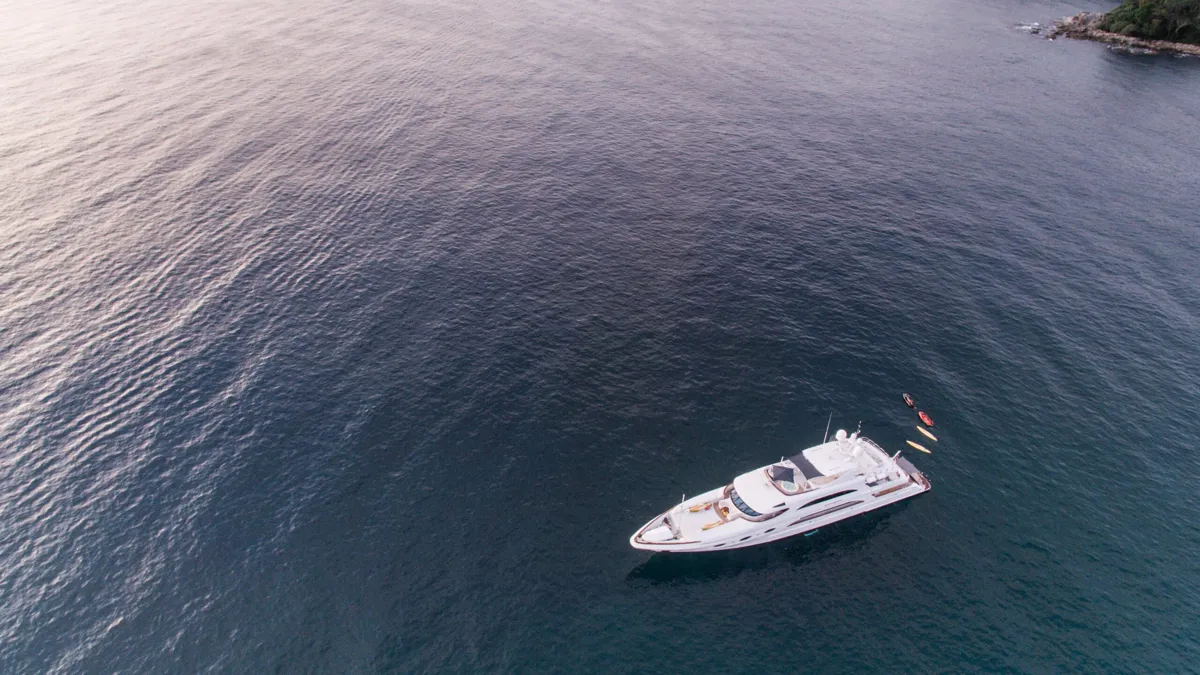 Aerial view of a luxury motor yacht anchored near a rocky coastline
